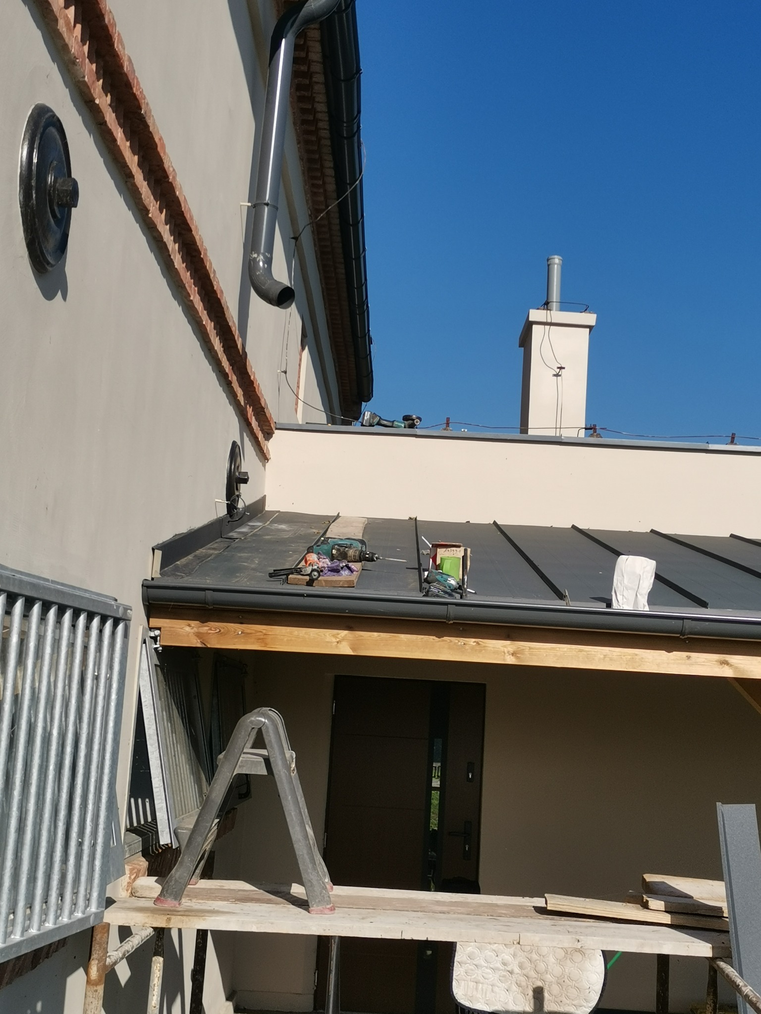 Montaż orynnowania i obróbek blacharskich na dachu domu jednorodzinnego, widoczna drabina i narzędzia pracy.