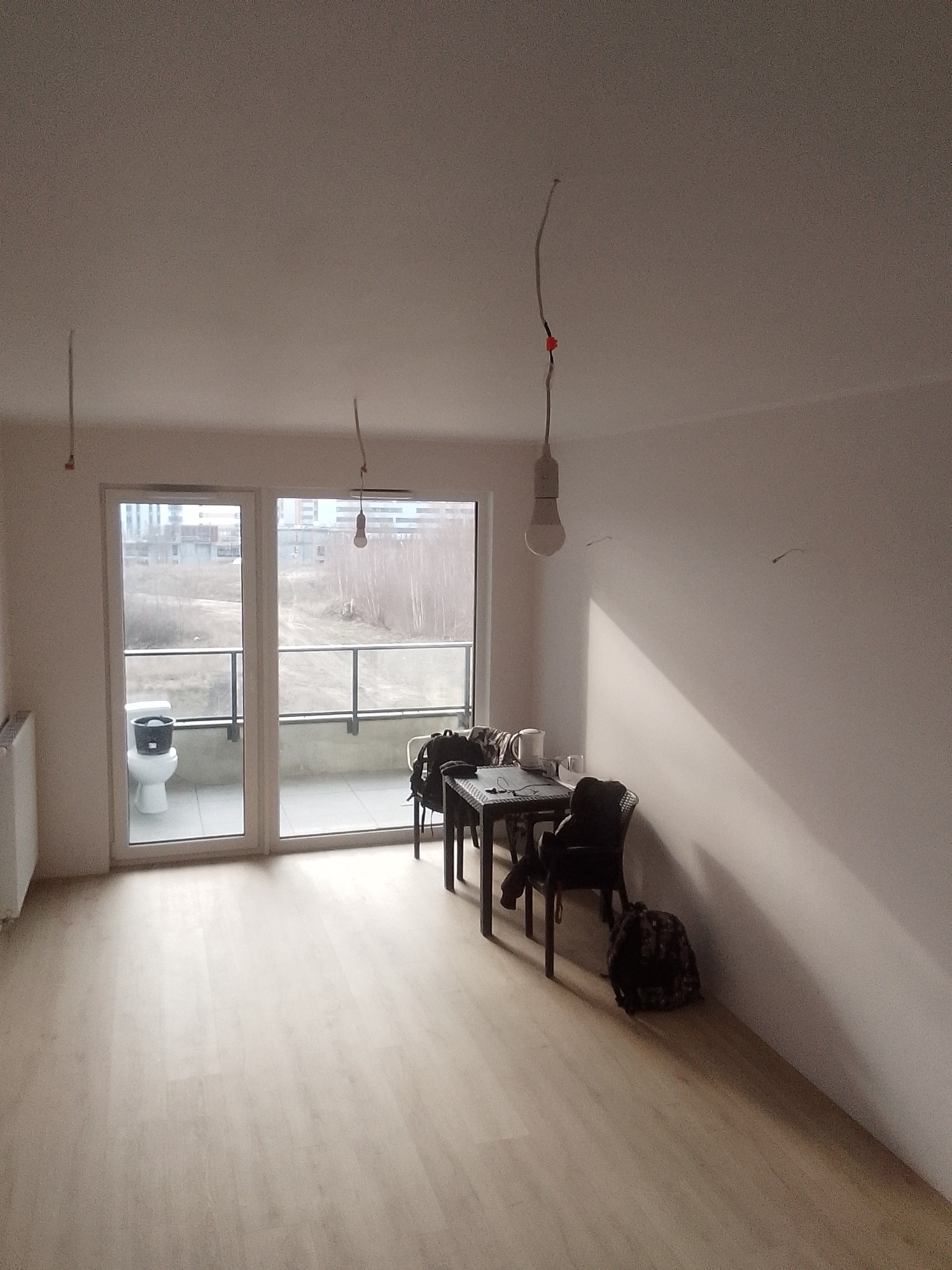 Wnętrze w trakcie remontu: gołe ściany, surowe żarówki na kablach, na balkonie toaleta z wiadrem w środku. Podłoga wyłożona panelami.