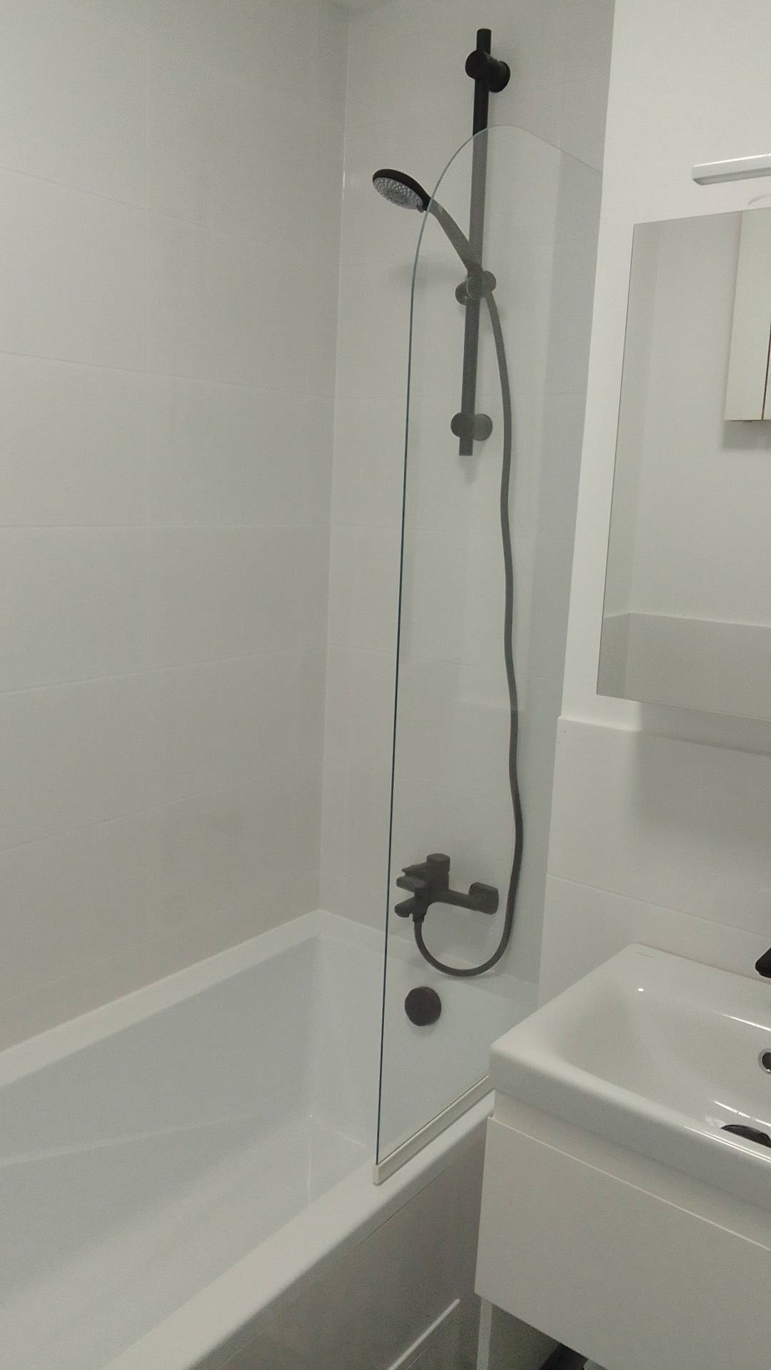 Nowoczesna łazienka z białą wanną, szklanym parawanem nawannowym i czarną armaturą, minimalistyczny design.