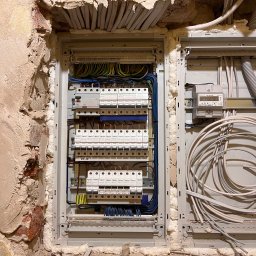 Yurii Tukalo Yurii_bud - Rozdzielnica elektryczna w trakcie montażu w ścianie w Sosnowcu, widoczne kable, zabezpieczenia i pianka montażowa uszczelniająca otwór w surowej ścianie.
