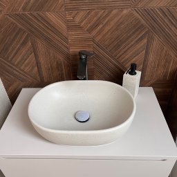 Yurii Tukalo Yurii_bud - Nowoczesna umywalka nablatowa z czarną armaturą i dozownikiem, na tle ściany z płytek imitujących drewno w geometryczny wzór. Minimalistyczny design.