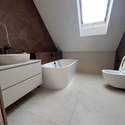 Yurii Tukalo Yurii_bud - Nowoczesna łazienka na poddaszu z oknem dachowym. Uwagę przykuwa ściana z dekoracyjną, drewnopodobną okładziną. Biała wanna wolnostojąca i umywalka nablatowa.
