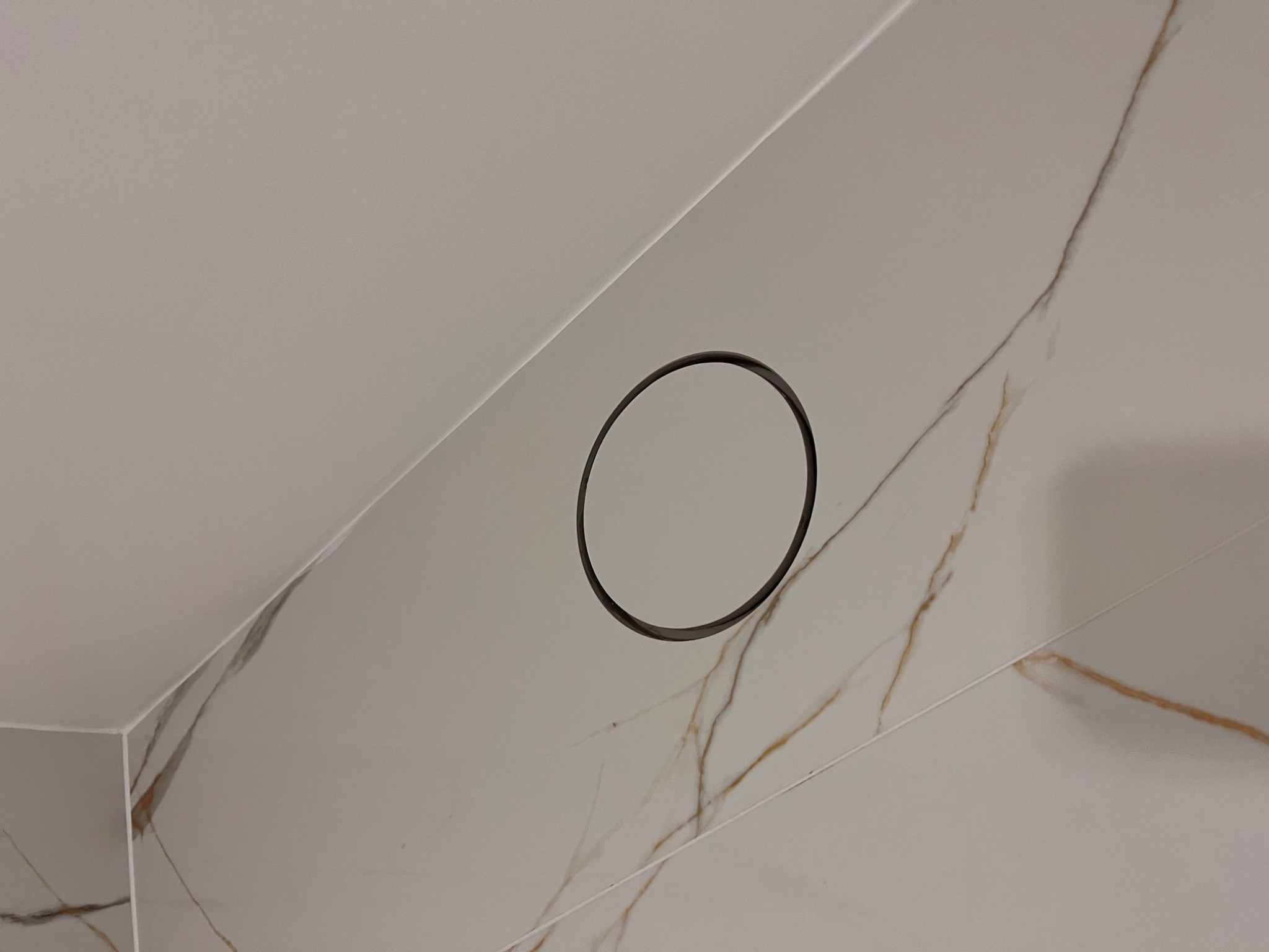 Białe płytki imitujące marmur z okrągłym odpływem liniowym w rogu łazienki. Minimalistyczny design, precyzyjne ułożenie płytek, nowoczesne wykończenie.