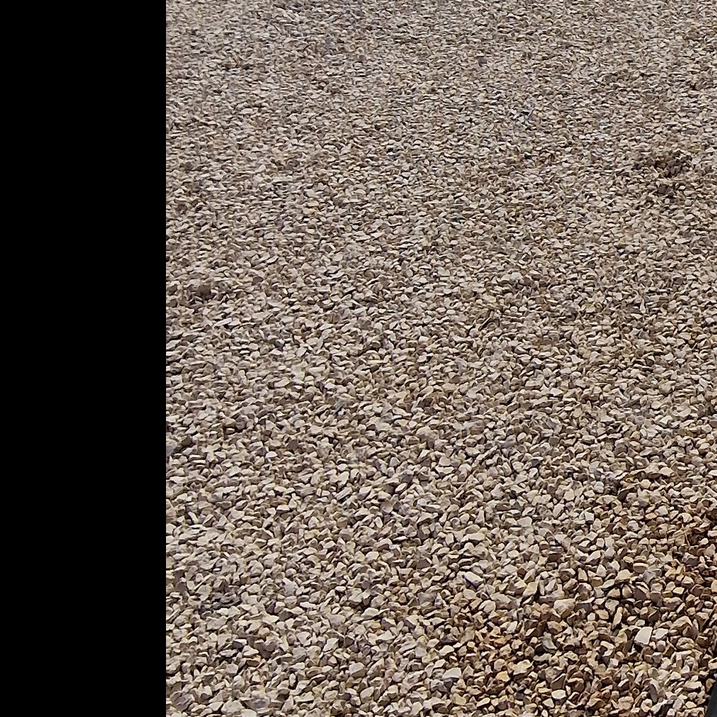 Beżowy żwir równomiernie pokrywa powierzchnię, tworząc utwardzoną drogę. Widoczny z bliska, ukazując strukturę i fakturę materiału.