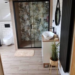 MIKUŚ USŁUGI REMONTOWE I WYKOŃCZENIOWE HYDRAULIKA PIOTR PALAT - Nowoczesna łazienka z kabiną prysznicową z motywem florystycznym, umywalką nablatową, czarnym grzejnikiem drabinkowym i drewnopodobną podłogą.