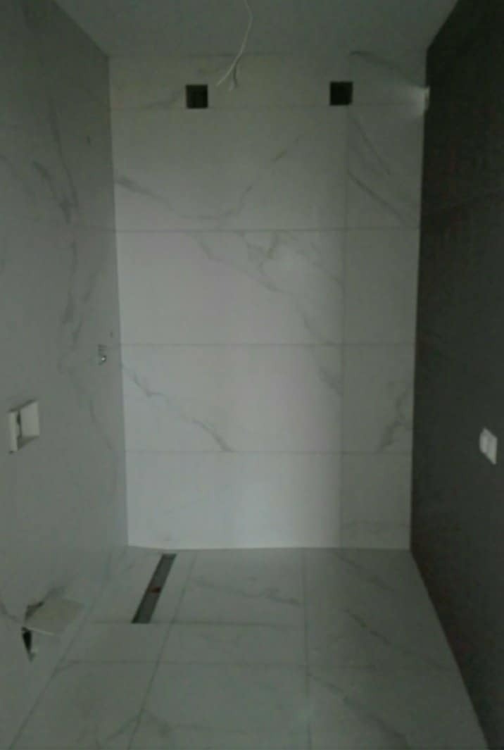 Wnętrze łazienki z wykończonymi ścianami i podłogą w białych płytkach imitujących marmur, widoczny odpływ liniowy w podłodze i przygotowane otwory na oświetlenie w suficie.