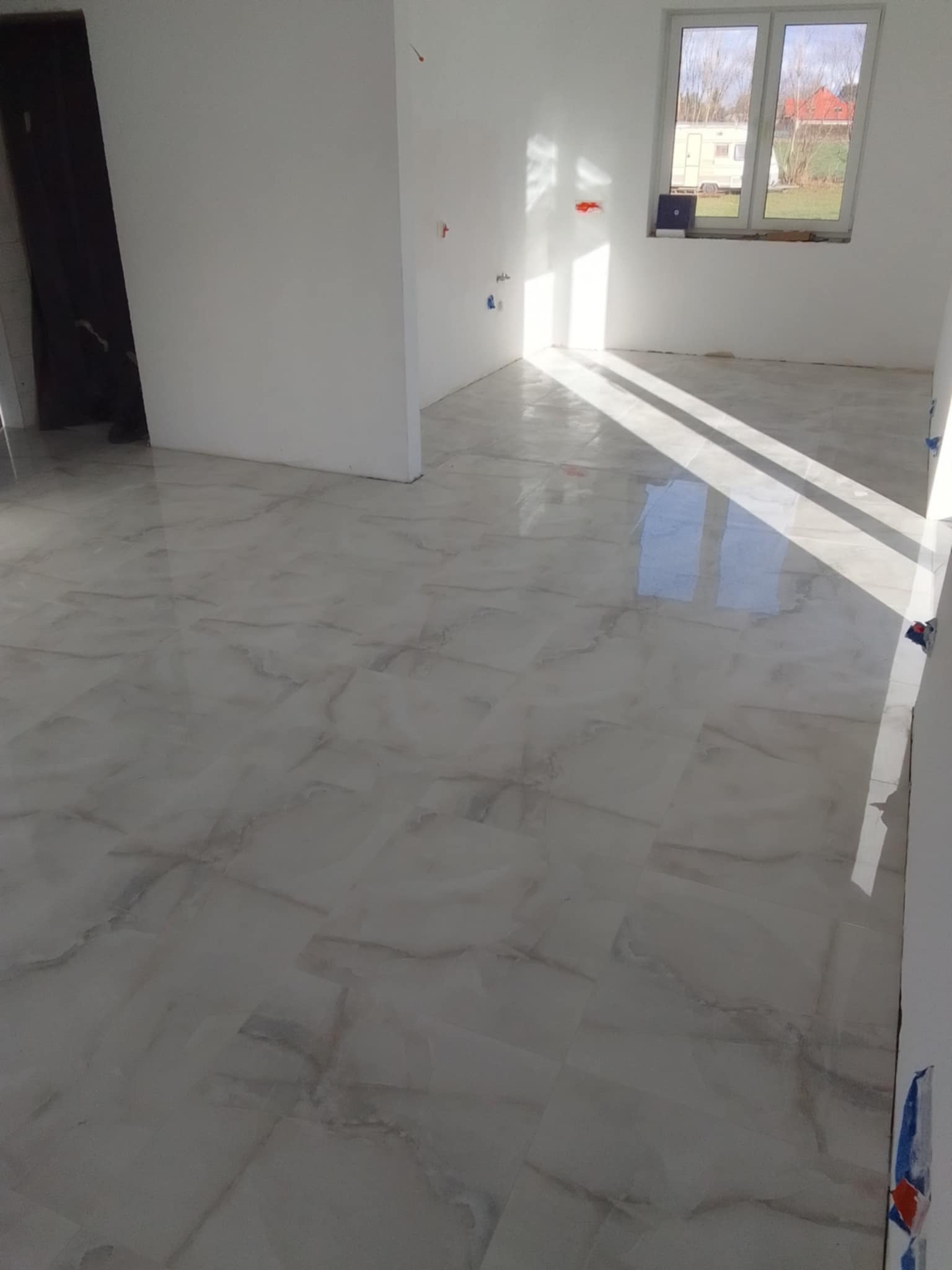 Jasne, marmurowe płytki podłogowe z widocznymi smugami światła słonecznego w nowym, pustym pokoju z białymi ścianami i oknem.