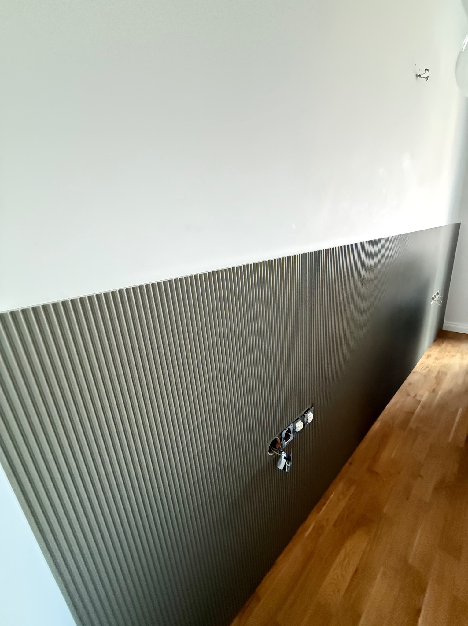 Montaż panelu dekoracyjnego z pionowymi żłobieniami na ścianie, widoczne gniazdka elektryczne w trakcie instalacji, parkiet na podłodze.