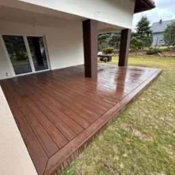 Zadaszony taras z deski kompozytowej w kolorze ciemnego drewna, wykończony obwodową deską, widok na ogród w pochmurny dzień.