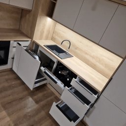 Linea Premium - Nowoczesna kuchnia z białymi frontami, drewnianym blatem i czarnym zlewozmywakiem, otwarte szuflady i zmywarka.