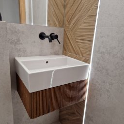 Linea Premium - Nowoczesna umywalka nablatowa z szafką z lamelami w łazience wykończonej płytkami imitującymi beton i drewnem ułożonym w geometryczny wzór.