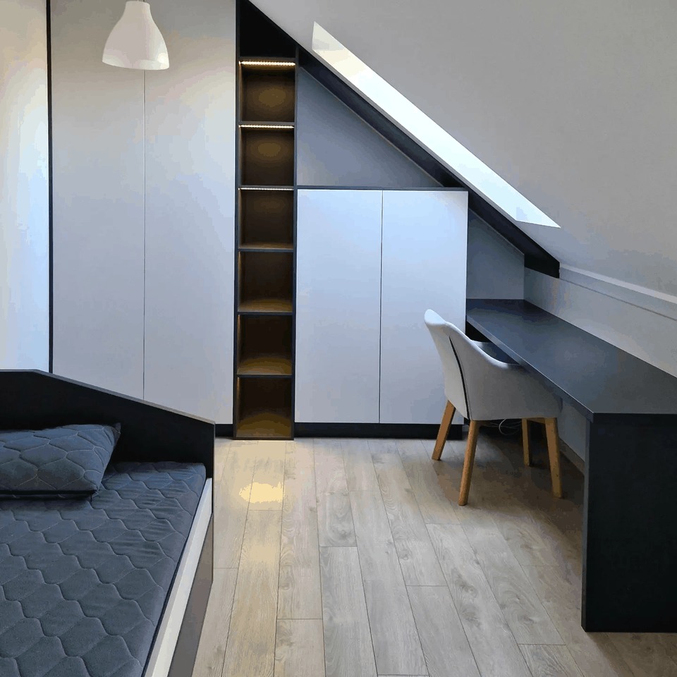 Pokój na poddaszu z zabudową meblową: białe szafy z czarnymi akcentami, regał z podświetleniem LED, biurko i tapicerowane krzesło na drewnianej podłodze.