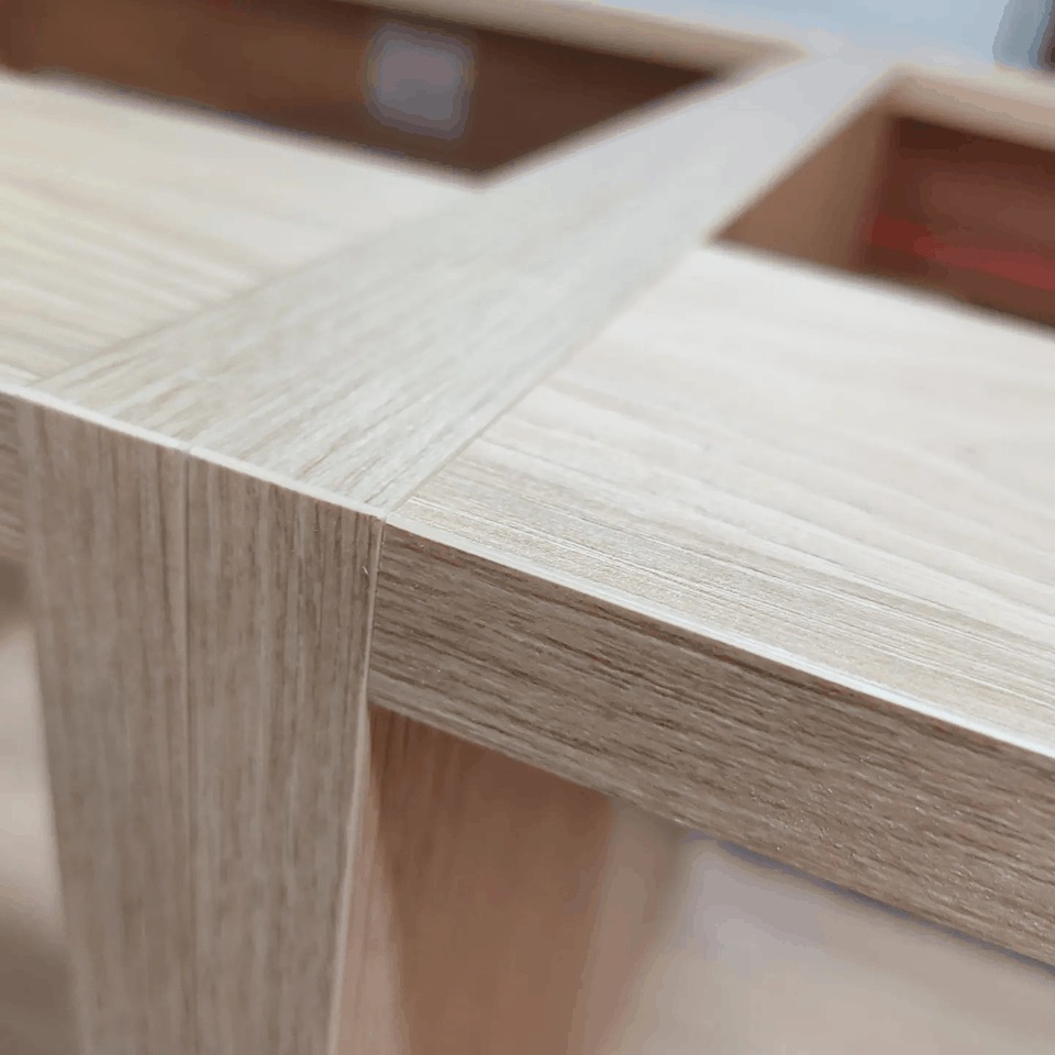 Detal drewnianej konstrukcji meblowej z jasnego drewna, ukazująca precyzyjne połączenie elementów pod kątem prostym.