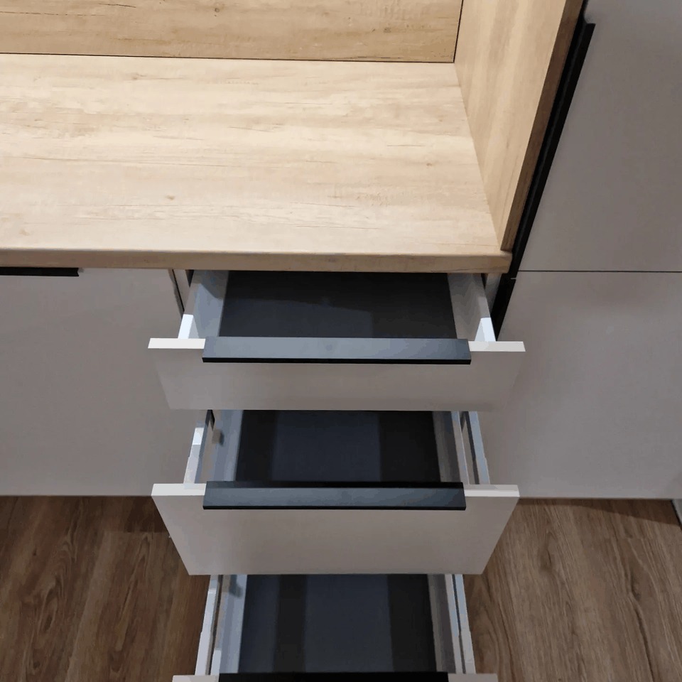 Wysuwane szuflady w zabudowie kuchennej z drewnianym blatem i minimalistycznymi, czarnymi uchwytami.