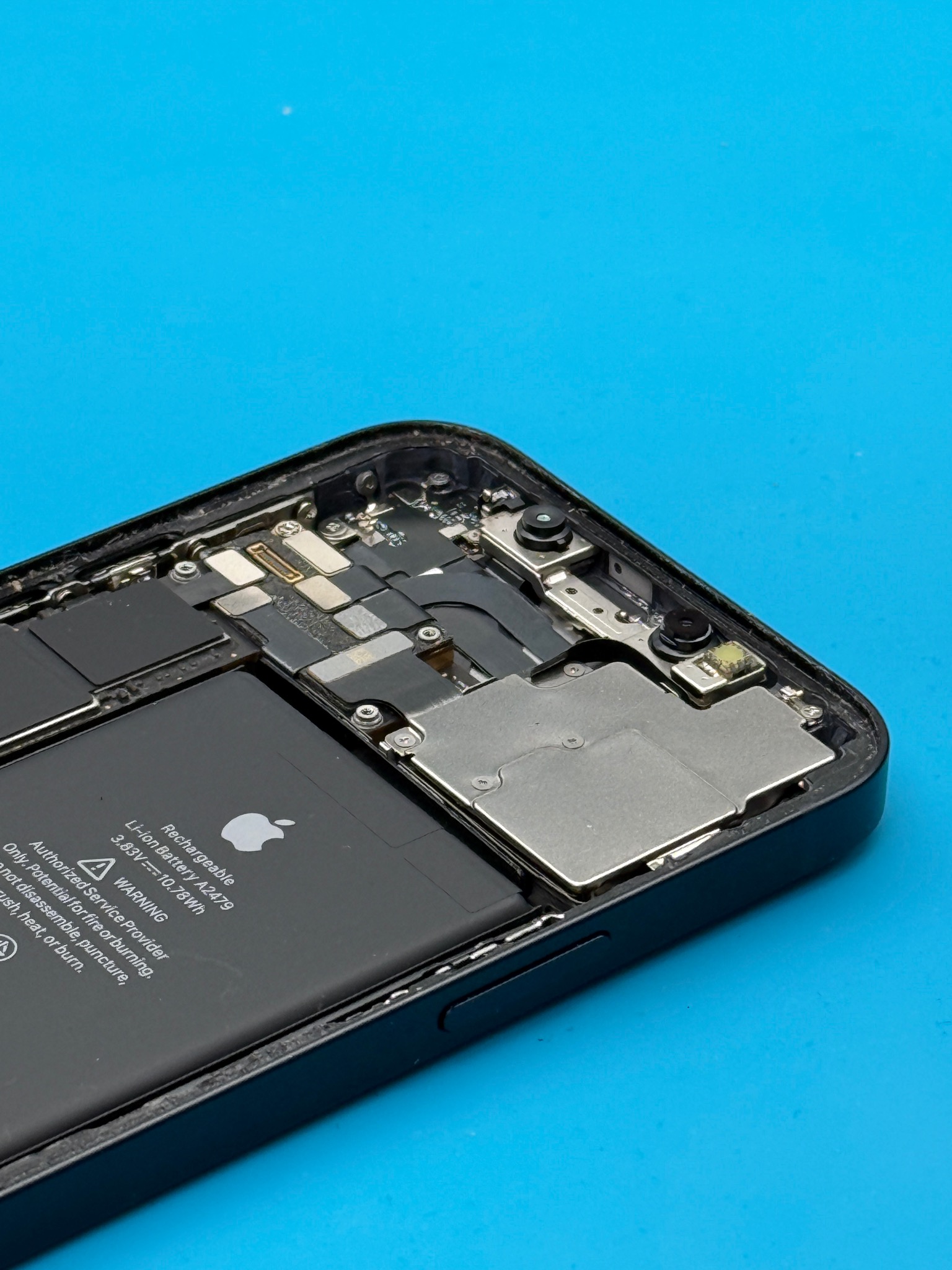 Otwarty iPhone z widoczną baterią i elementami wewnętrznymi na niebieskim tle. Widoczne ślady naprawy i demontażu.