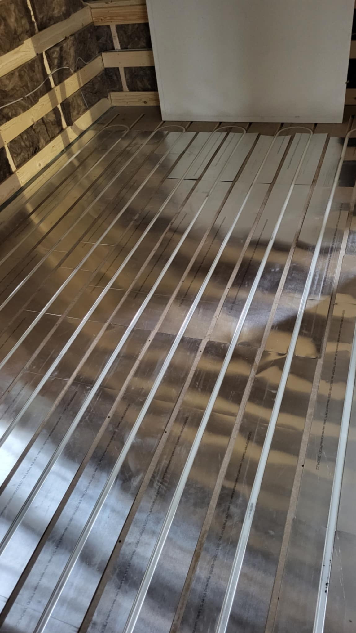 Metalowe profile pod ogrzewanie podłogowe ułożone na izolacji poddasza, widoczne drewniane elementy konstrukcyjne ściany.