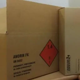 Kartonowe opakowanie z oznaczeniami ADR dla materiałów wybuchowych (klasa 1.4S), etykieta 'świece przeciw gryzoniom' i logo firmy Dasco Electronic na mniejszym kartonie obok.