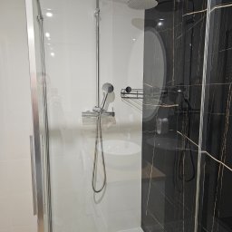 Shany up - Nowoczesna kabina prysznicowa z chromowaną armaturą na tle białych płytek i ściany z czarnego marmuru z złotymi żyłami.