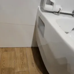 Nowoczesna, podwieszana toaleta z otwartą klapą, widoczna na tle białych płytek ściennych i drewnopodobnej podłogi.