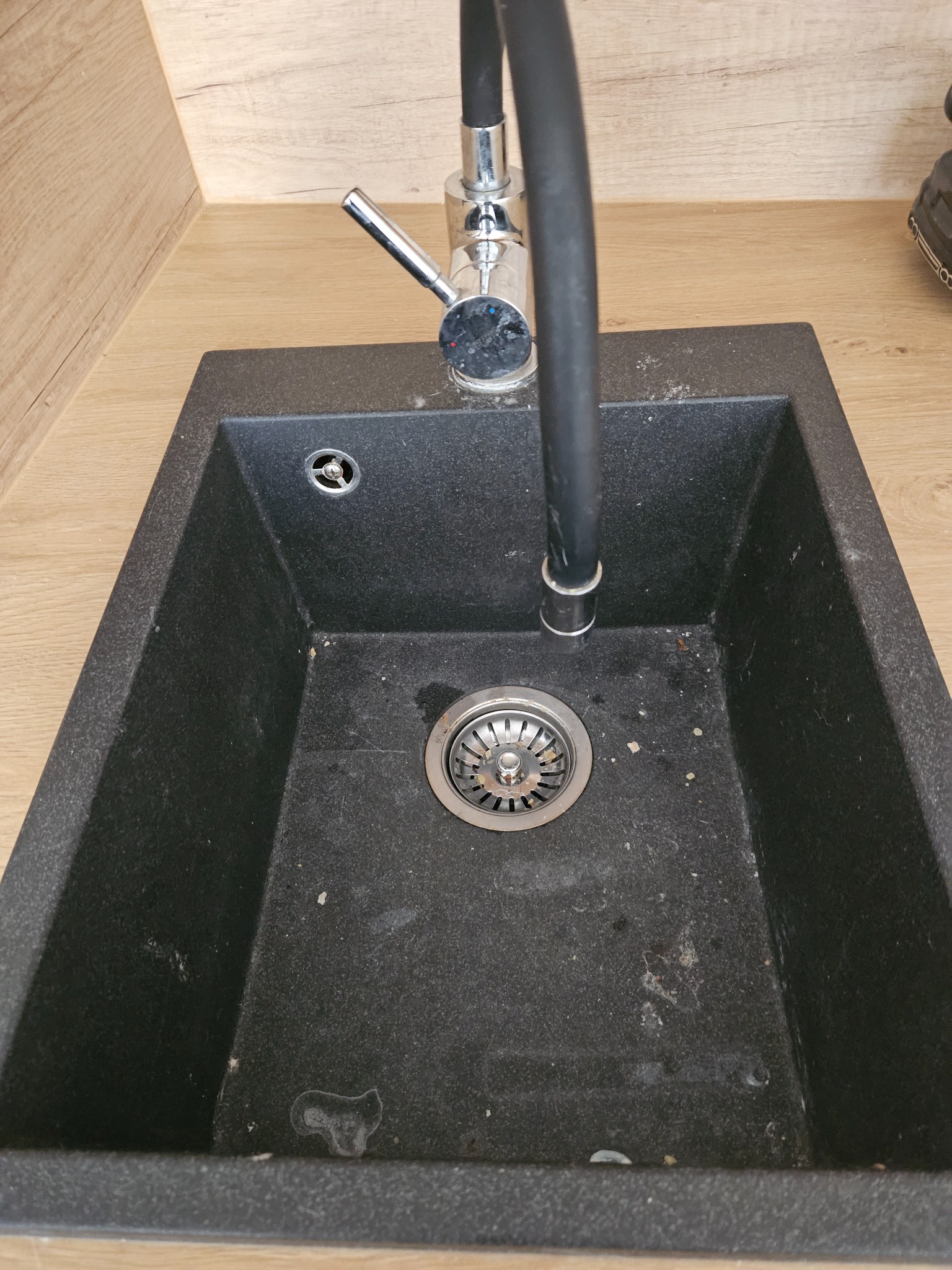 Czarny, granitowy zlew kuchenny z chromowaną baterią, widoczne ślady użytkowania i drobne zabrudzenia.