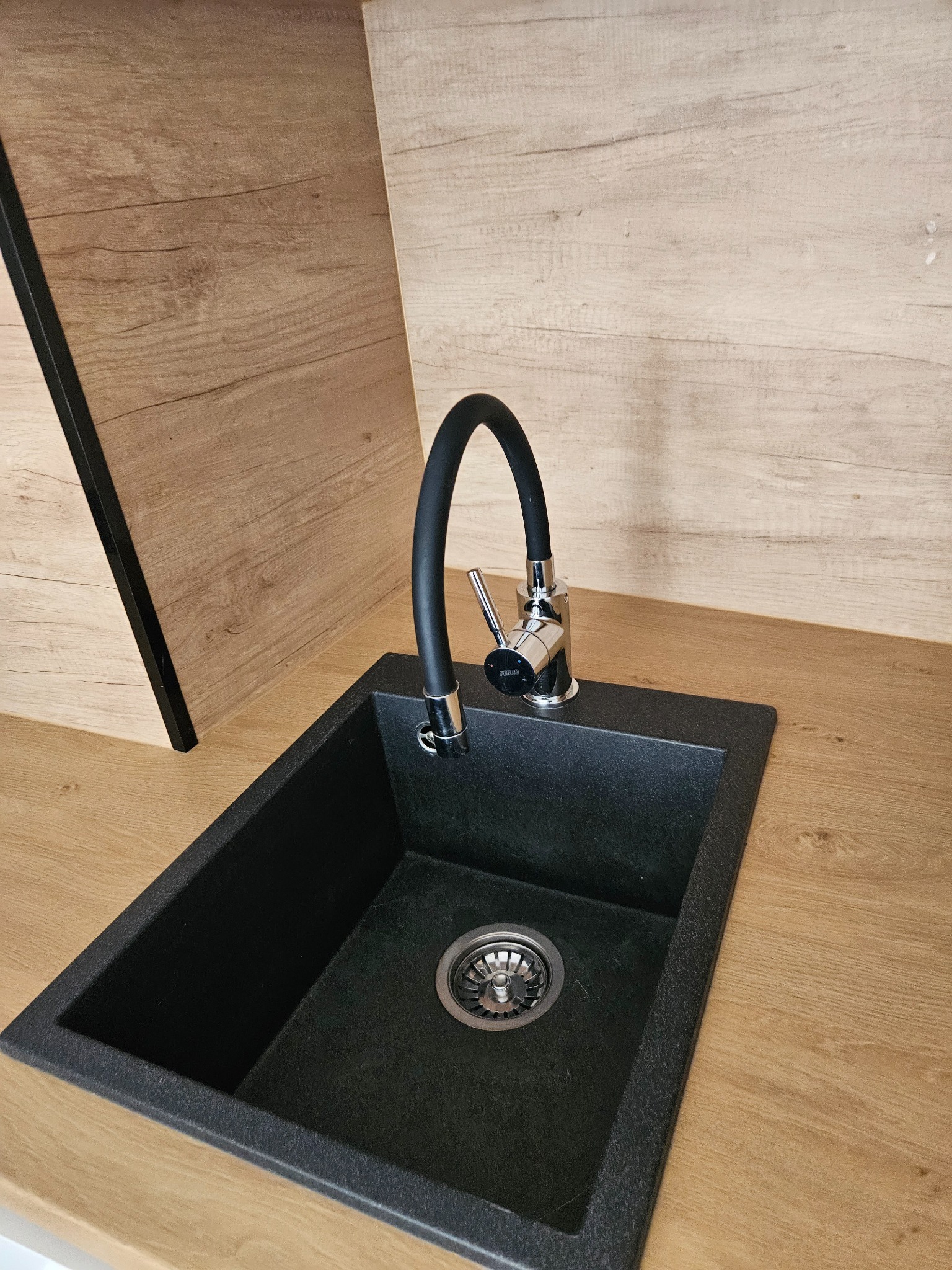 Czarny, granitowy zlew z chromowaną baterią w nowoczesnej kuchni z drewnianymi frontami.