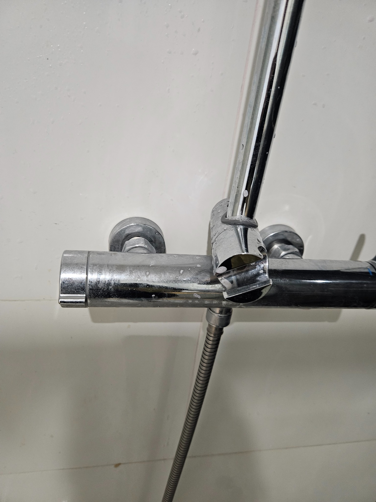 Bateria prysznicowa z chromowaną powierzchnią, widoczne ślady po twardej wodzie i osadach, zbliżenie na armaturę w łazience na tle białej ściany.