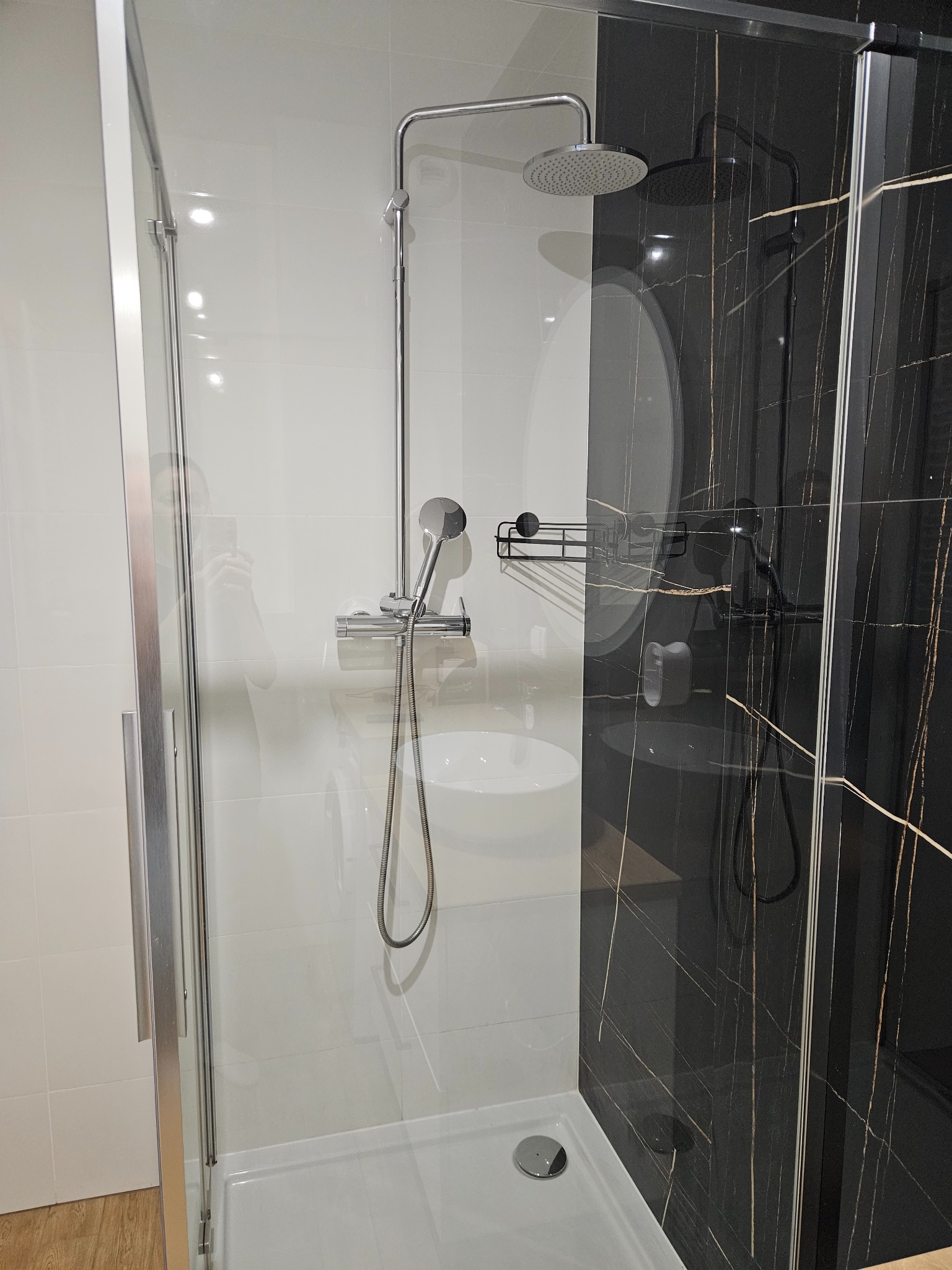 Nowoczesna kabina prysznicowa z chromowaną armaturą na tle białych płytek i ściany z czarnego marmuru z złotymi żyłami.