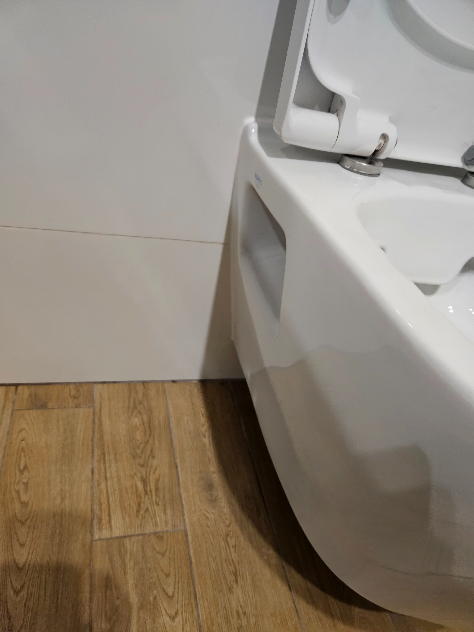 Nowoczesna, podwieszana toaleta z otwartą klapą, widoczna na tle białych płytek ściennych i drewnopodobnej podłogi.