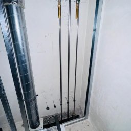 TECHNOLOGY BAU SPÓŁKA Z OGRANICZONĄ ODPOWIEDZIALNOŚCIĄ - Surowe wnętrze w trakcie prac wykończeniowych: pionowe rury instalacji wodnej z zaworami odcinającymi, widoczne elementy konstrukcji ścian działowych oraz fragment kanału wentylacyjnego.