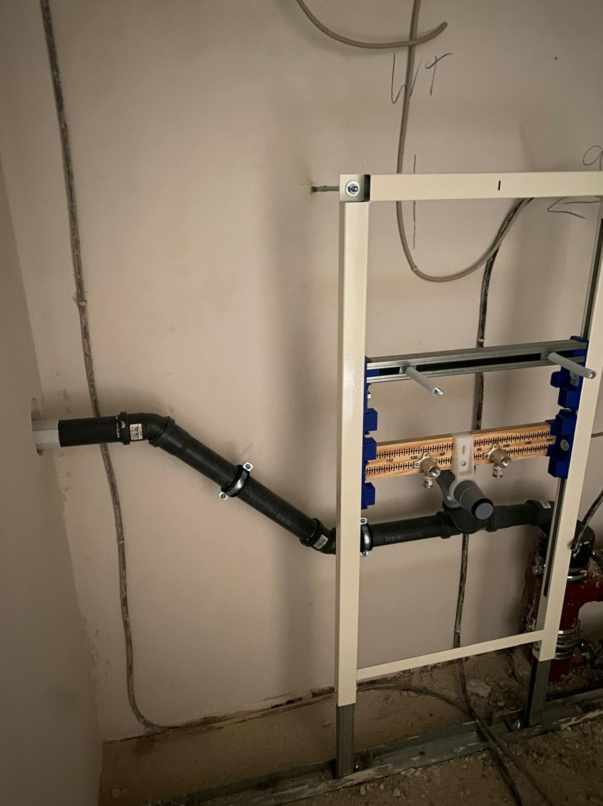 Stelaż podtynkowy WC z podłączeniami kanalizacyjnymi i wodnymi w trakcie montażu, widoczne rury odpływowe i instalacja wodna w surowym stanie.