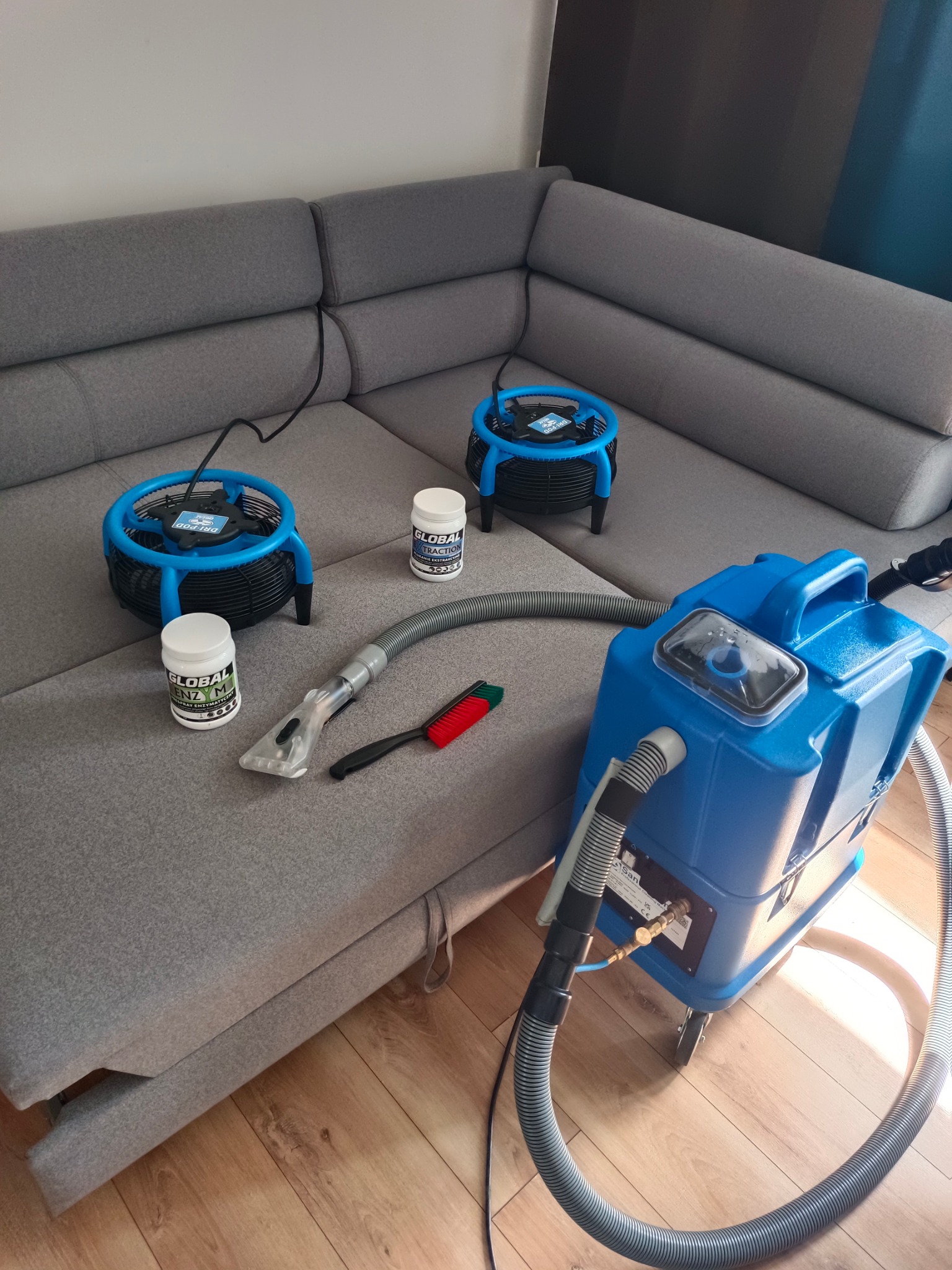 Sprzęt i środki do prania narożnika: niebieski ekstraktor, suszarki podłogowe, szczotka i preparaty Global Enz M i Extraction. Profesjonalne pranie tapicerki.