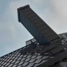 Nisko kątowe ujęcie ciemnej, błyszczącej dachówki ceramicznej z zamontowanym, prostokątnym kominkiem wentylacyjnym z metalową kratką wentylacyjną, na tle pochmurnego nieba.