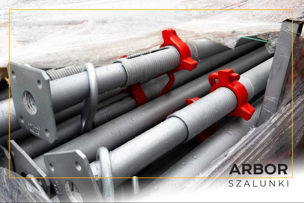 Stalowe stemple budowlane z czerwonymi nakrętkami regulacyjnymi, zapakowane w folię, widoczne ślady wilgoci.