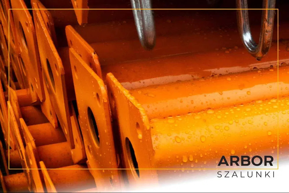 Pomarańczowe, metalowe elementy szalunkowe z widocznymi kroplami wody, ułożone warstwami.