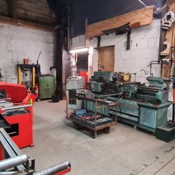 Z.P.H.U KRZYSZTOF LEJMAN - Warsztat ślusarski z maszynami do obróbki metalu, w tle widoczna piła taśmowa do metalu w kolorze czerwonym, tokarka, frezarka i inne narzędzia.