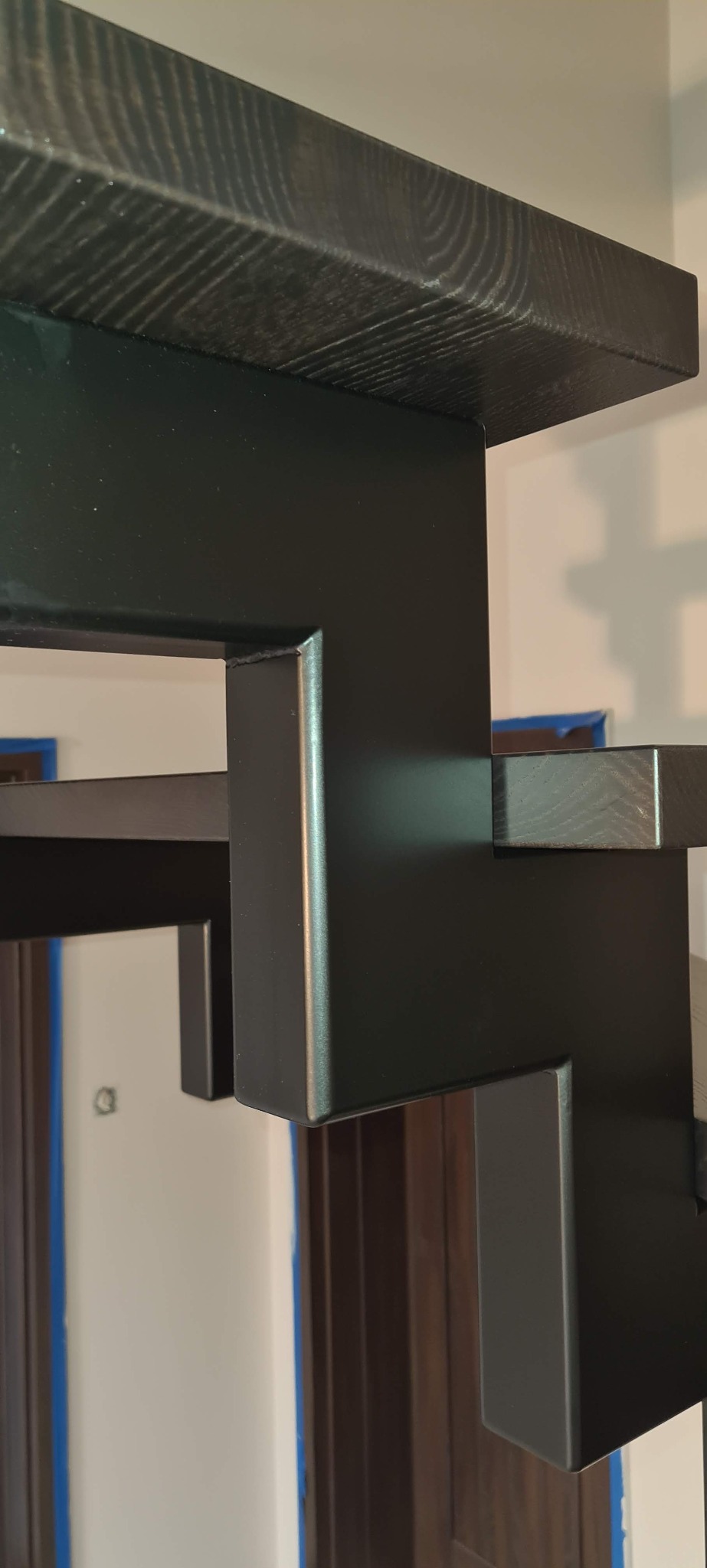 Fragment czarnych, metalowych schodów z drewnianymi stopniami o wyraźnym usłojeniu, widoczne drzwi w tle.