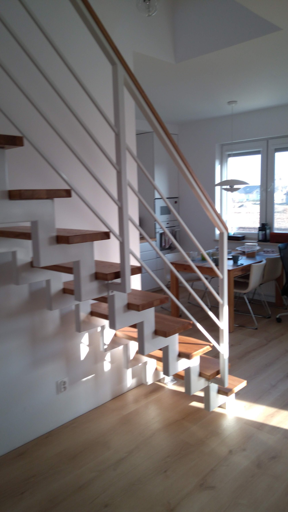 Nowoczesne schody metalowe z drewnianymi stopniami i białą balustradą w jasnym wnętrzu domu.