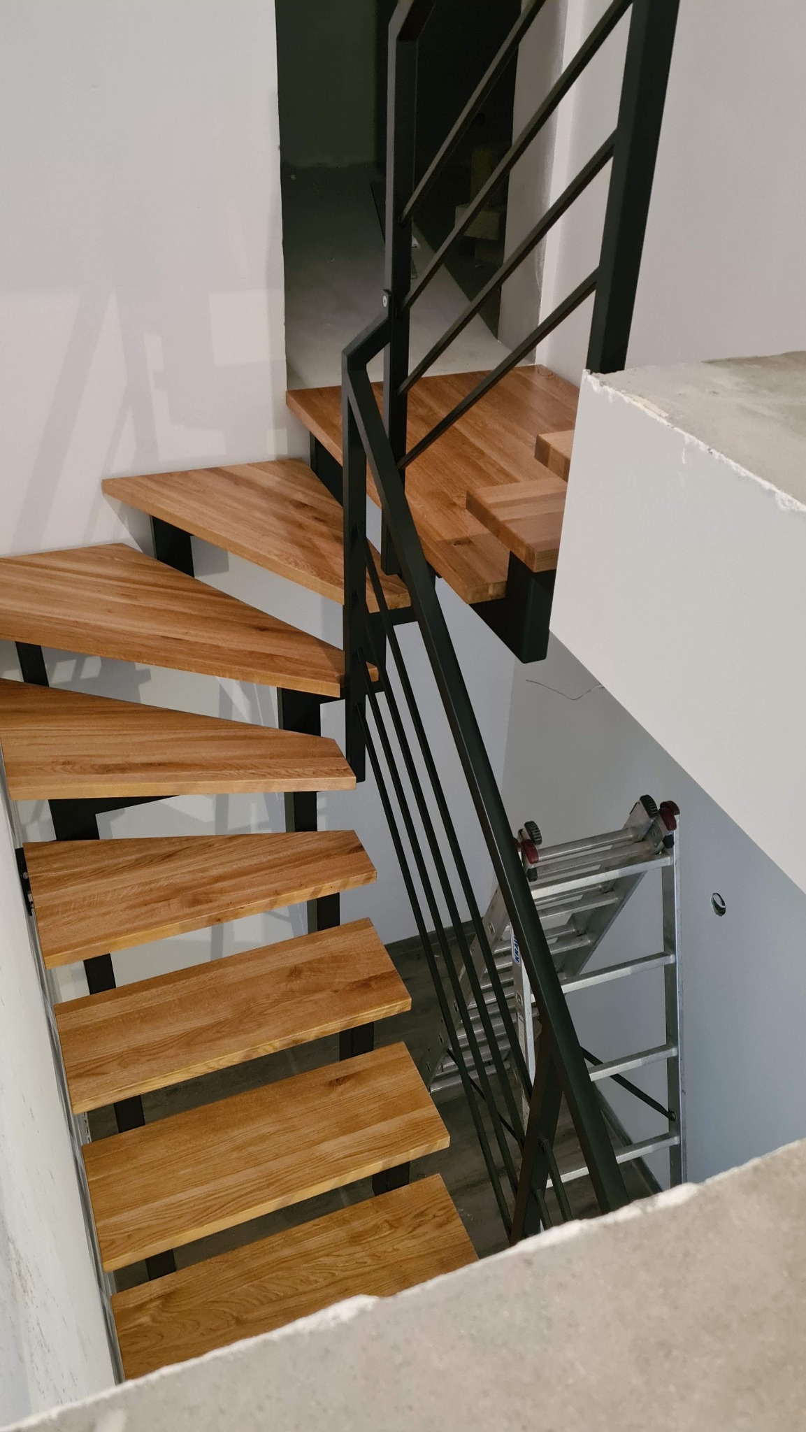 Nowoczesne schody z drewnianymi stopniami i czarną metalową balustradą, widok z góry, drabina w tle.