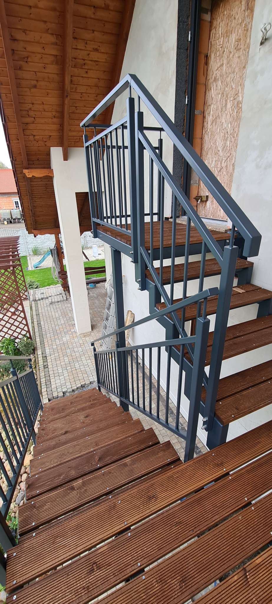 Zewnętrzne schody z drewnianymi stopniami i metalową, szarą balustradą, prowadzące w dół, widok z góry.