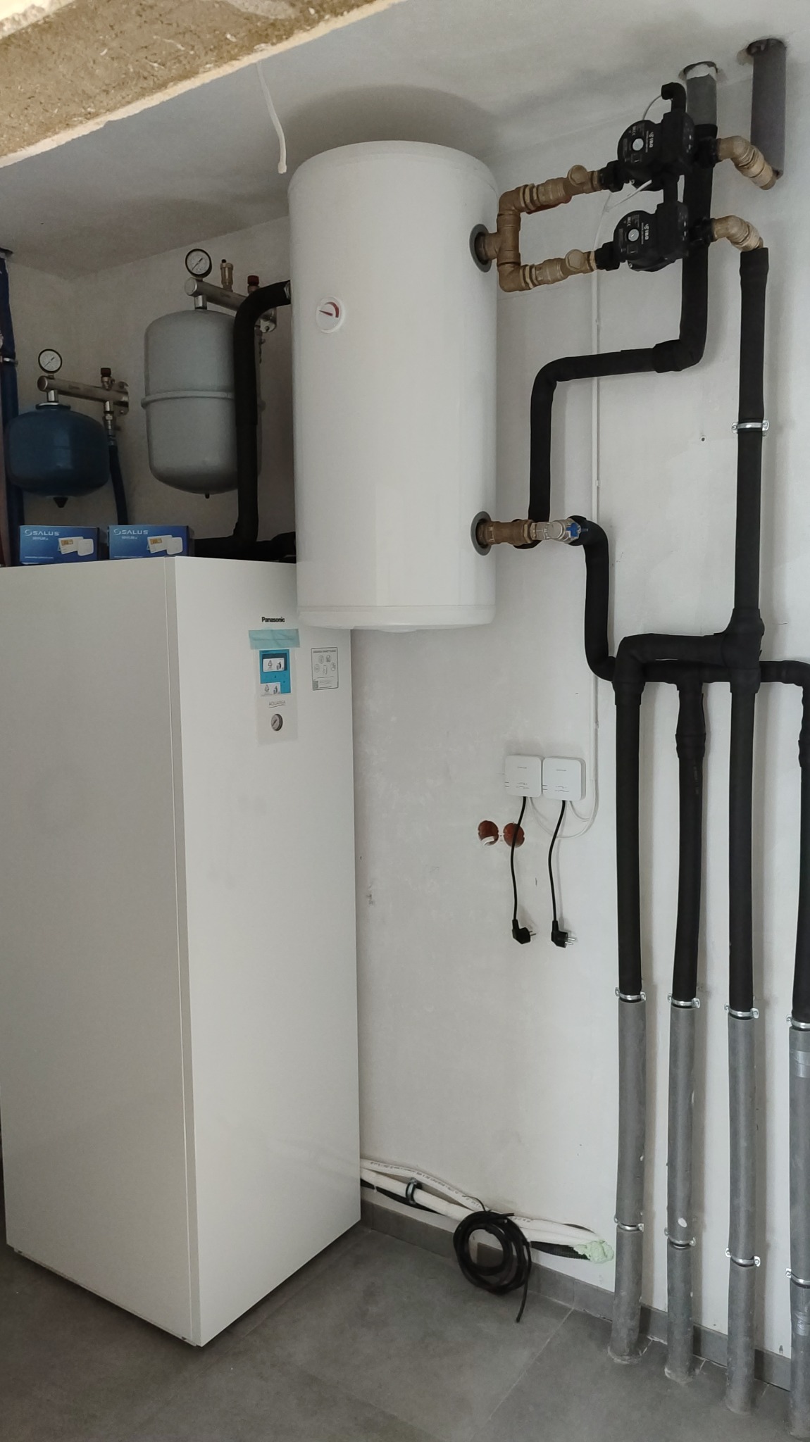 Nowoczesna instalacja grzewcza z pompą ciepła Panasonic Aquarea, zbiornikiem buforowym i rozbudowanym systemem rur miedzianych oraz czarnych rur grzewczych w kotłowni.