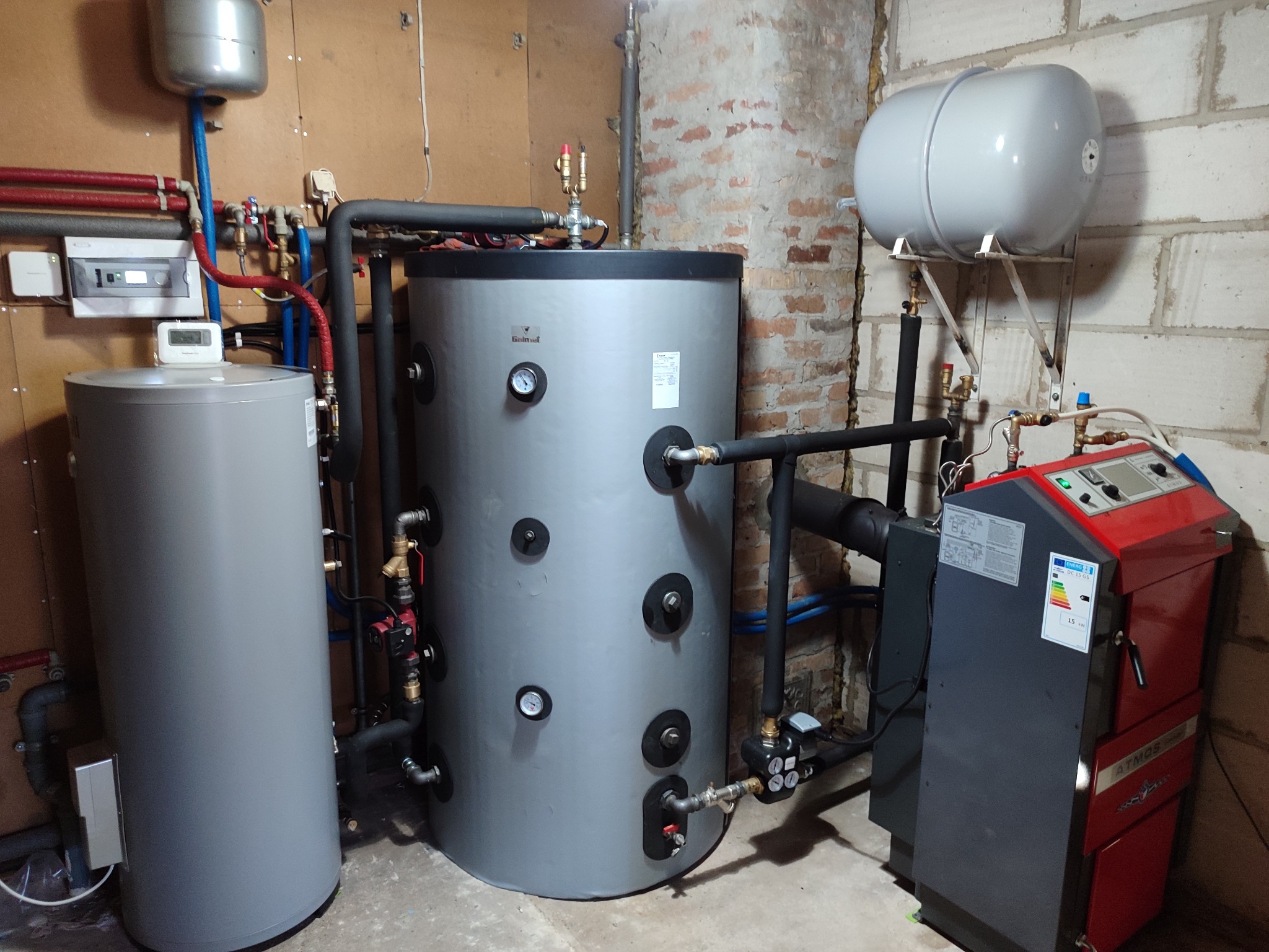 Instalacja centralnego ogrzewania z kotłem na paliwo stałe, zbiornikiem akumulacyjnym i naczyniem przeponowym w kotłowni z elementami murowanej ściany z cegły.