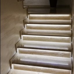 DM usługi elektryczne - Marmurowe schody z podświetleniem LED na każdym stopniu, prowadzące do góry, z rośliną doniczkową na górnym podeście.