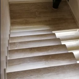 DM usługi elektryczne - Schody z podświetleniem LED na każdym stopniu, wykonane z beżowego kamienia, z rośliną doniczkową na górnym podeście.