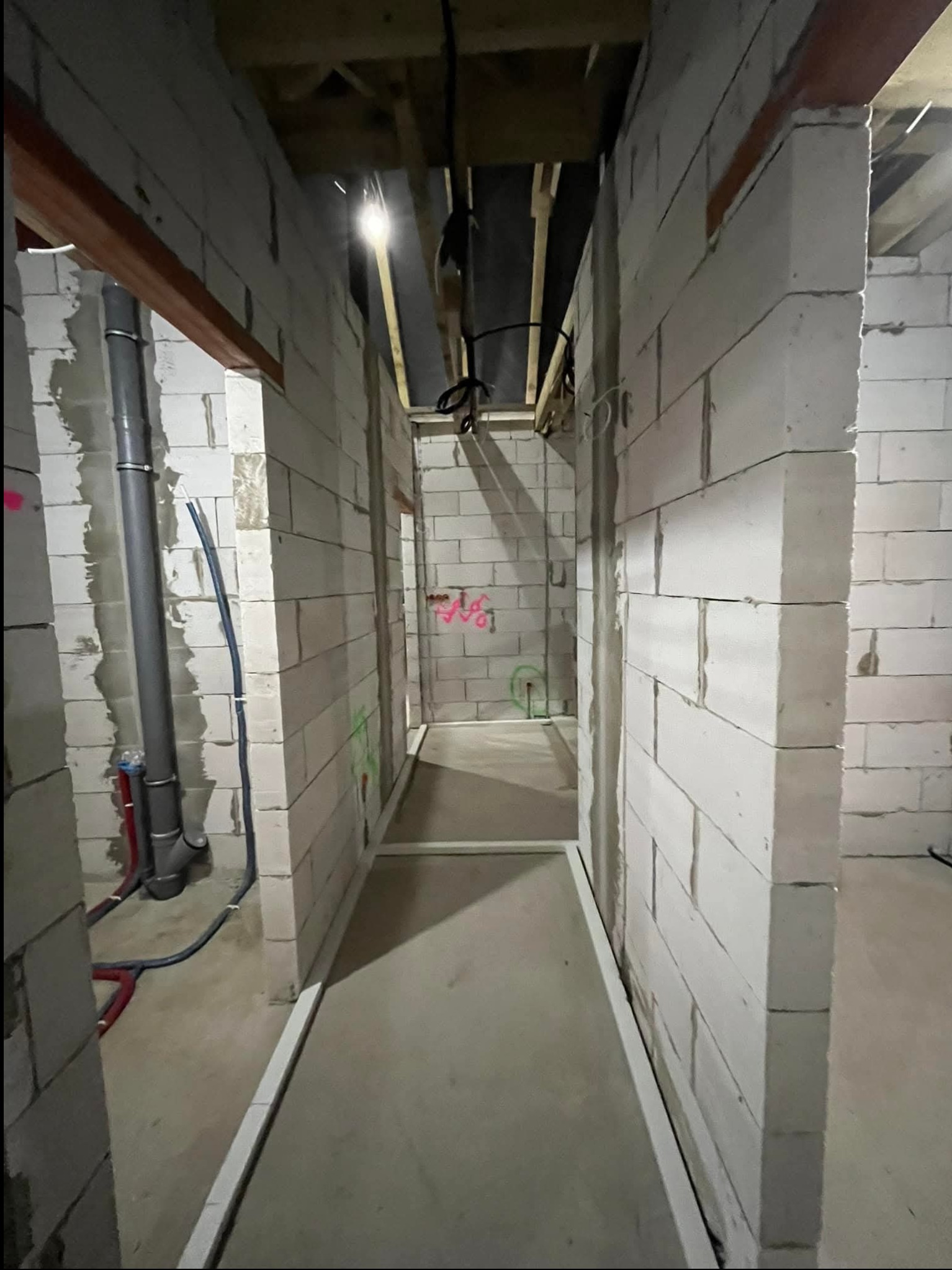 Wnętrze w trakcie budowy z widocznymi przewodami elektrycznymi i rurami kanalizacyjnymi, ściany z białych bloczków, surowy stan wykończenia.