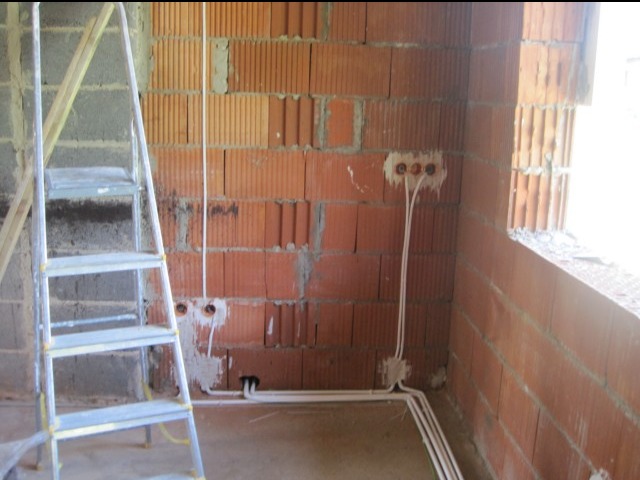 Wewnętrzna instalacja elektryczna w surowym stanie: widoczne przewody w peszlach, puszki elektryczne w ścianie z cegły dziurawki oraz aluminiowa drabina przystawna.