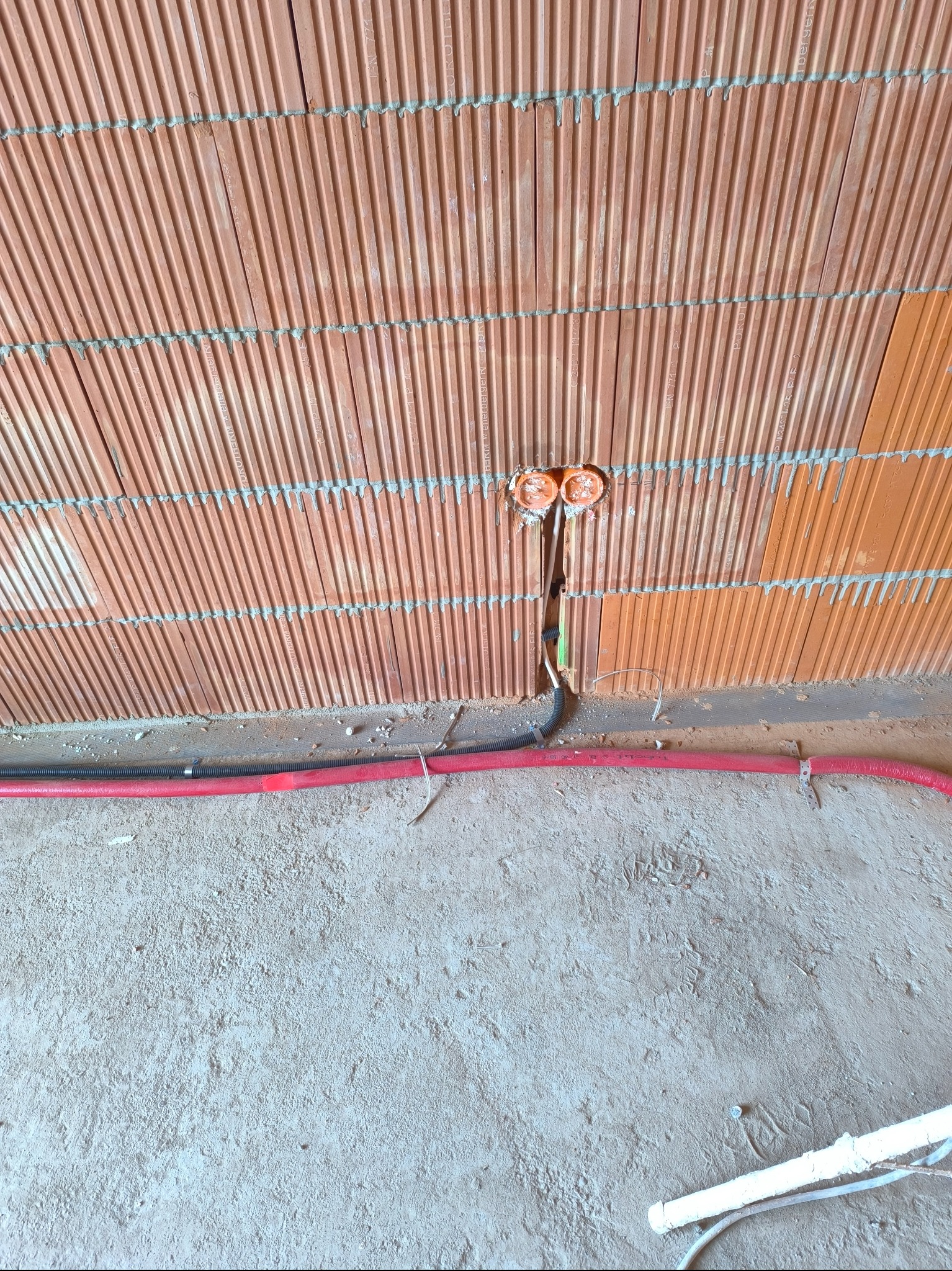 Instalacja elektryczna w trakcie budowy w Namysłowie: widoczne puszki instalacyjne w ścianie z cegły kratówki oraz przewody elektryczne poprowadzone wzdłuż podłogi.