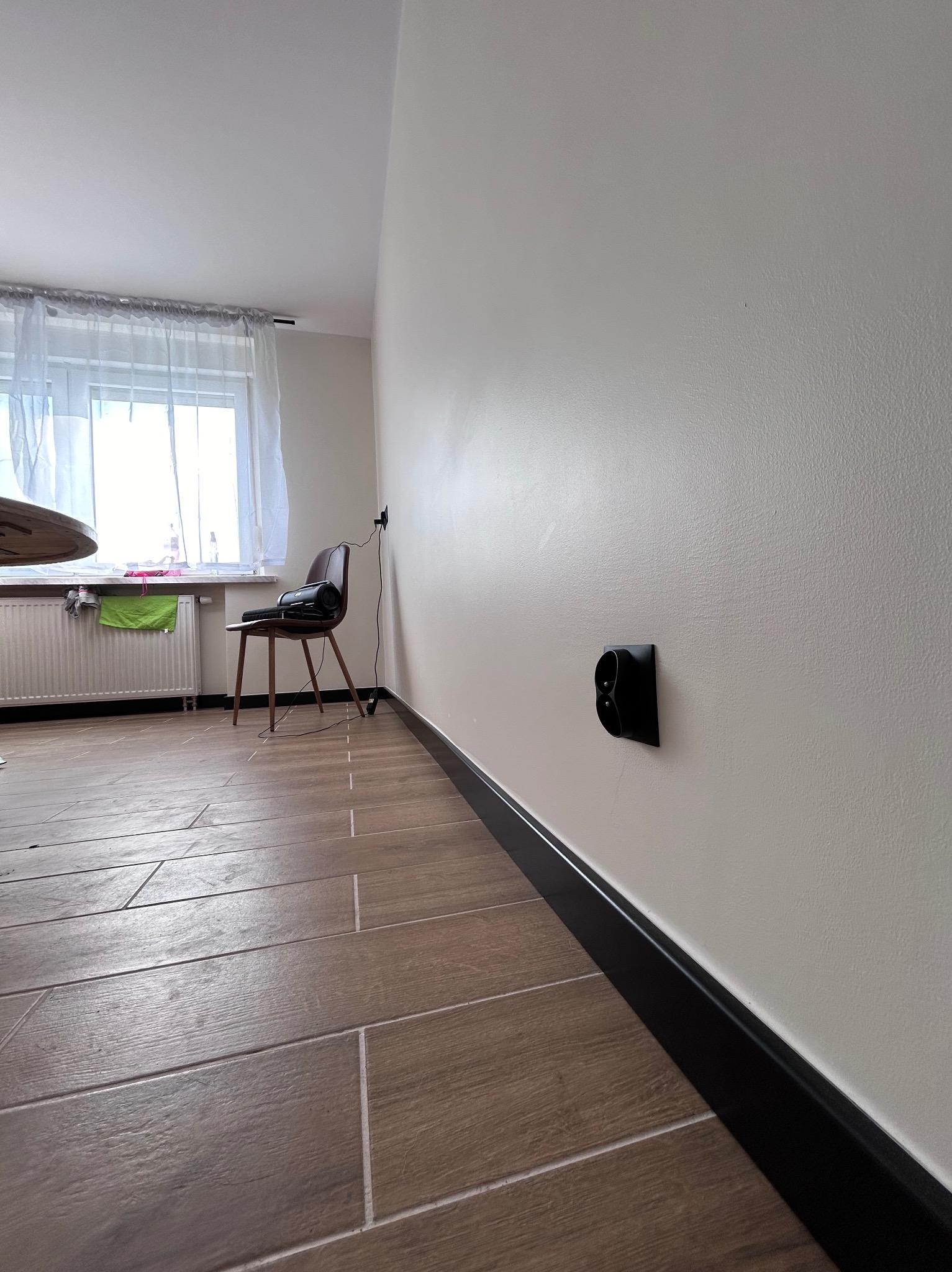 Nowoczesne gniazdko elektryczne w kolorze czarnym, zamontowane w jasnej ścianie nad czarną listwą przypodłogową w nowym mieszkaniu, widok z perspektywy podłogi.