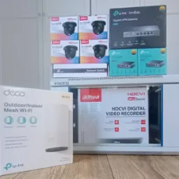 Pudełka z kamerami, rejestratorem wideo, routerem VPN, switchem sieciowym i punktem dostępowym Wi-Fi, ułożone na półce, gotowe do instalacji.