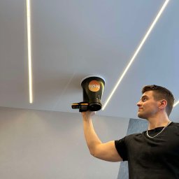 Hydraulik Tomasz Bereza - Mężczyzna mierzy przepływ powietrza anemometrem marki Testo przy suficie z oświetleniem liniowym LED.