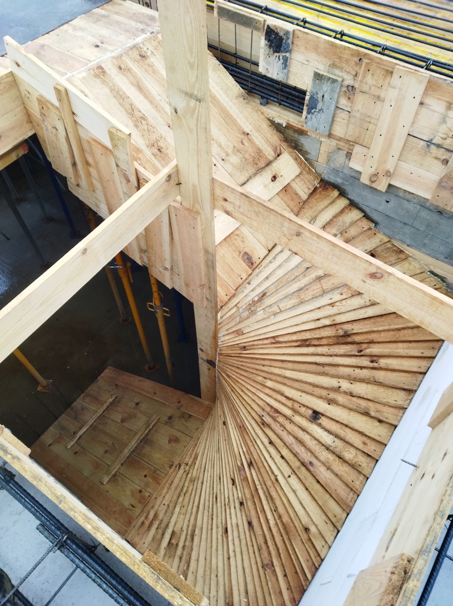 Szalunek spiralnych schodów z desek, widok z góry. Konstrukcja wsparta na metalowych stemplach. W tle widoczne zbrojenie i betonowy fundament.